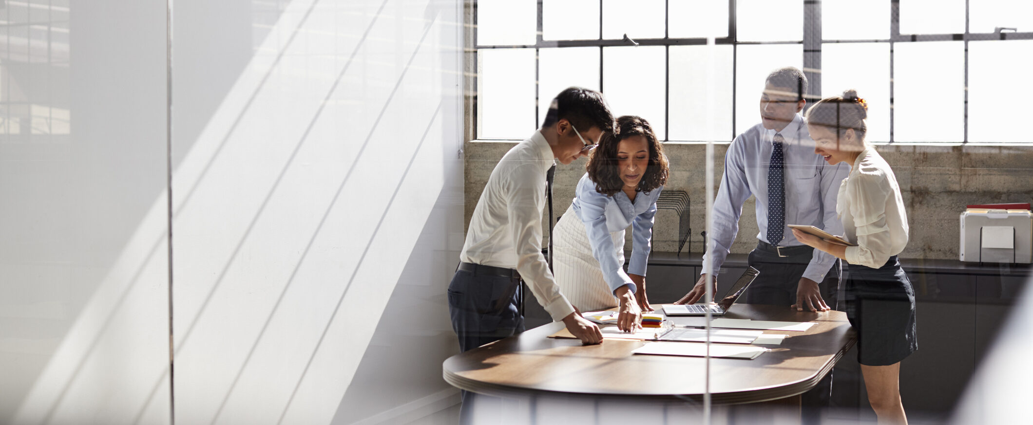 Four business colleagues stand talking in a meeting room